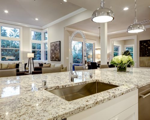 White Kitchen Design In New Luxurious Home White kitchen design features large bar style kitchen island with granite countertop illuminated by modern pendant lights. Northwest USA